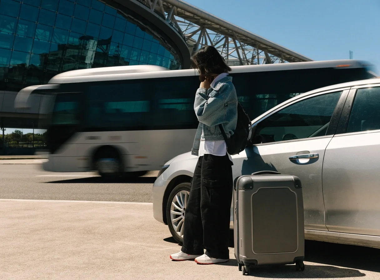 Traveller with suitcase beside parked car while shuttle passes