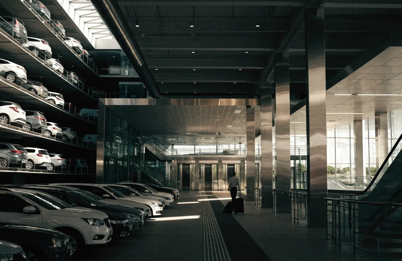 Traveller with roller bag walking along covered parking walkway toward lifts